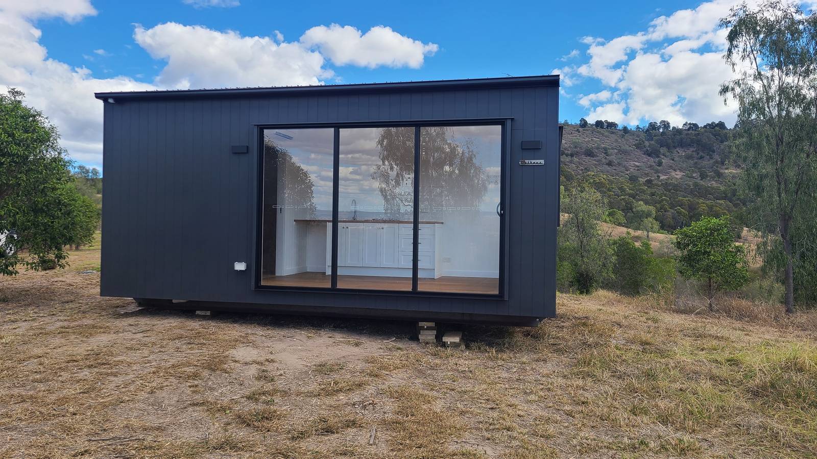 A dark modular home with a wide glass slider on a hillside block
