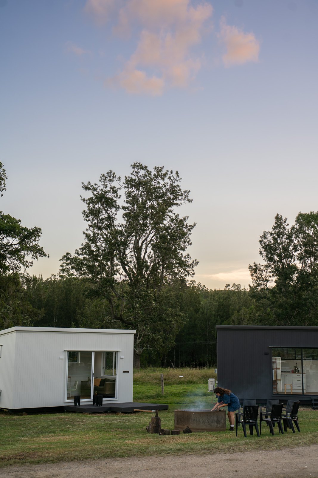 A white and a dark second home in a paddock at dusk, chairs around a fire pit