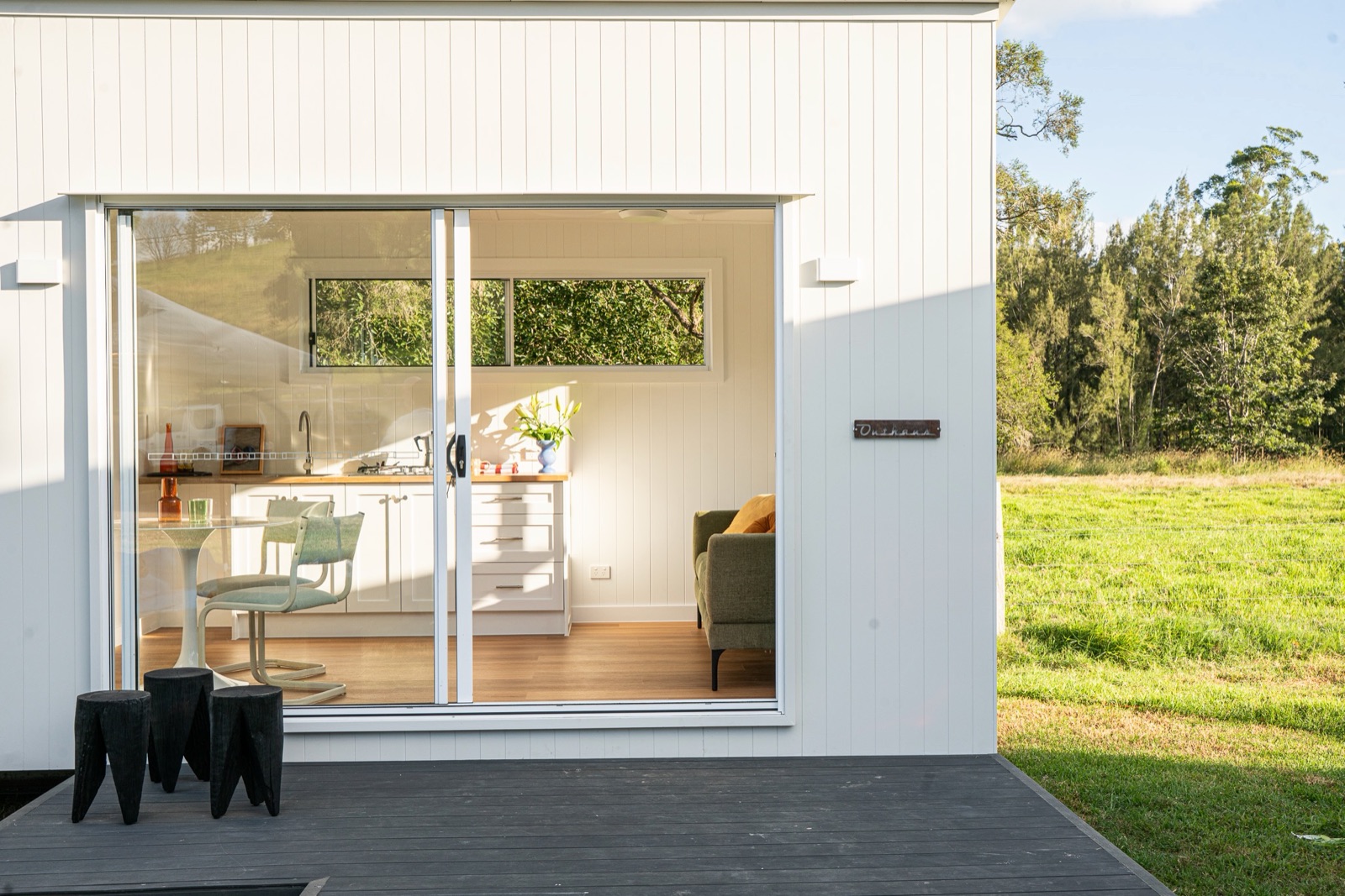 A white second home with its doors open, a green paddock beside it